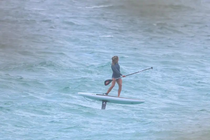 A foiler strides forward on a white board, paddle planted ahead in the chop