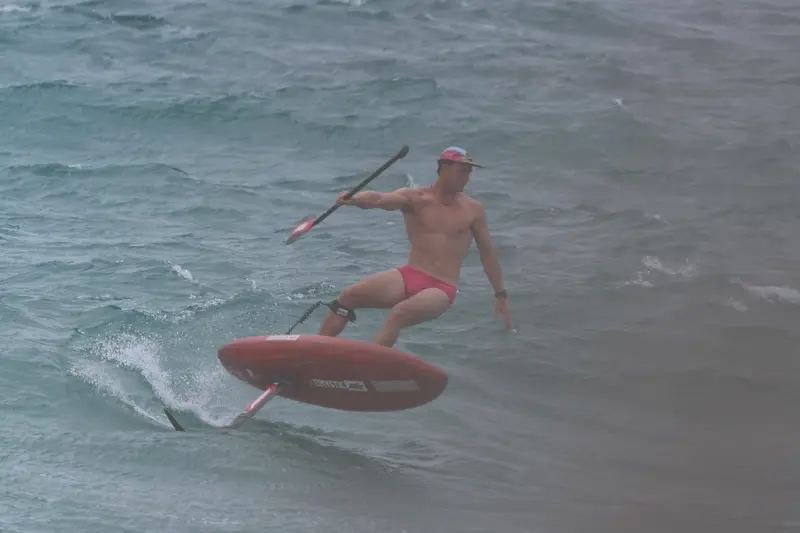 A foiler in a cap carves a red board through grey-blue swell